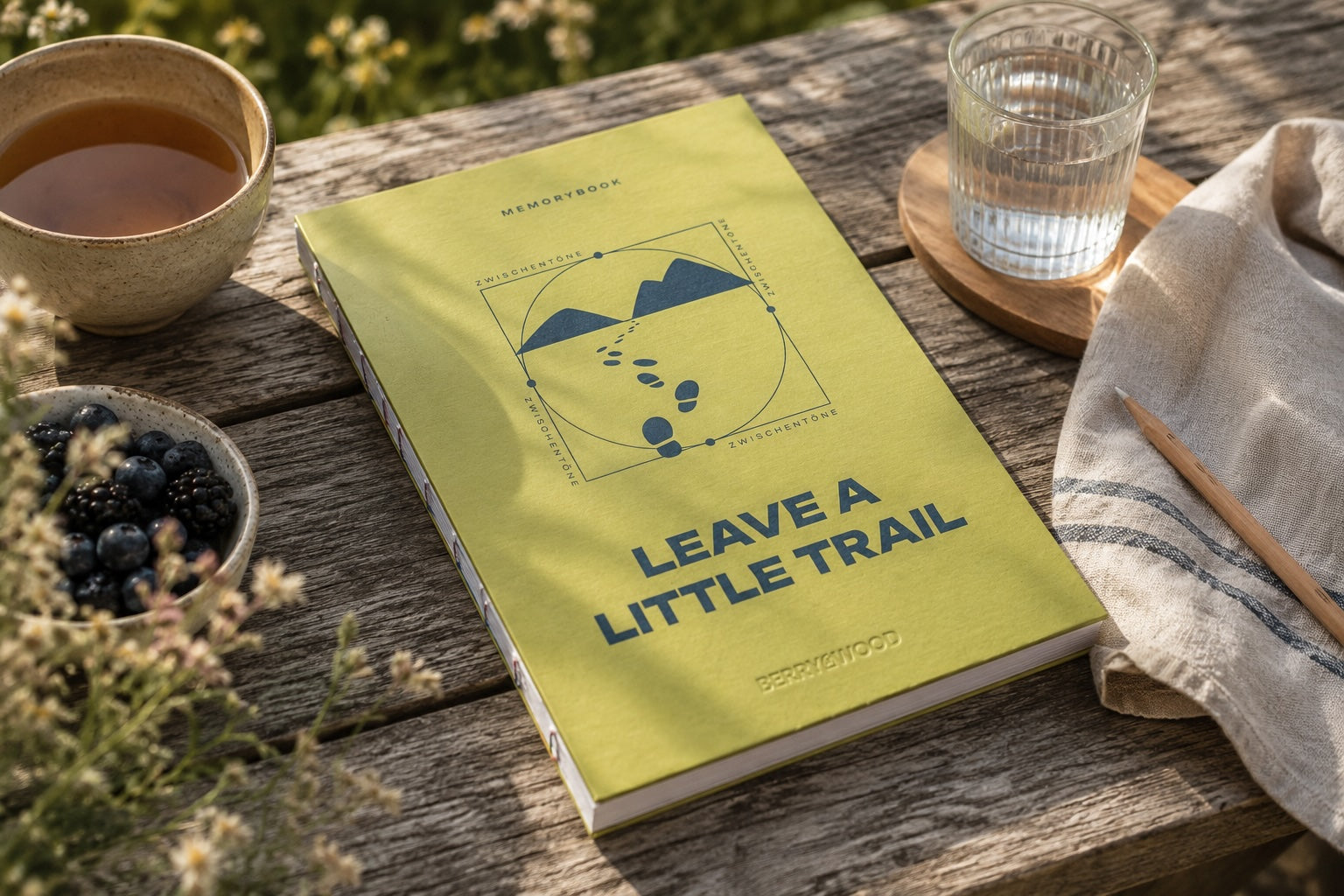 Leave a Little Trail Bullet Journal A5 in Limette/Blau auf einem Gartentisch mit Tee, Beeren und Bleistift
