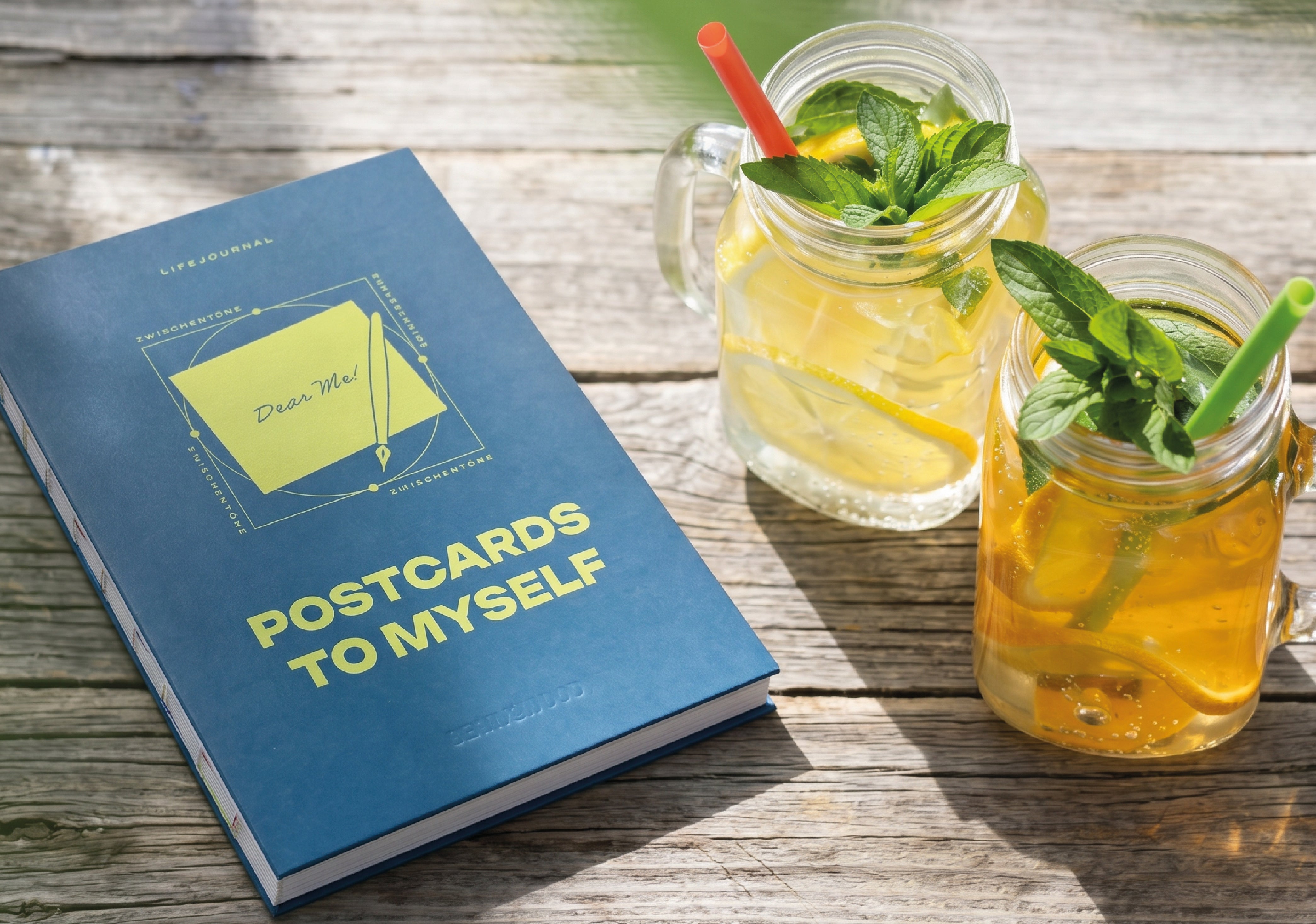 Postcards to Myself Lifejournal zur Selbstreflexion – Journal auf einem Holztisch draußen, daneben Eistee mit Minze und Zitrone